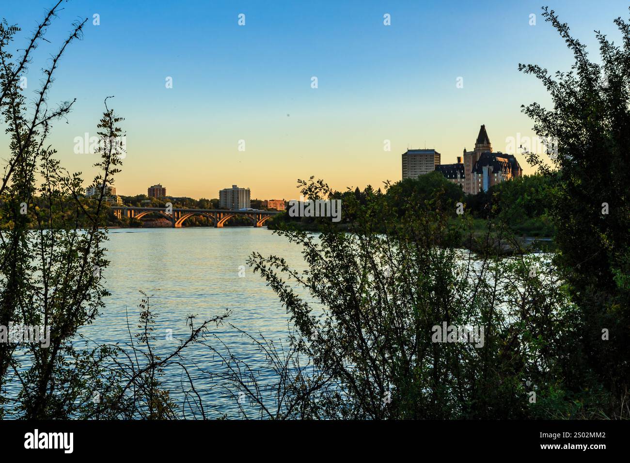 A beautiful view of a city with a river in the background. The sky is blue and the sun is setting Stock Photo