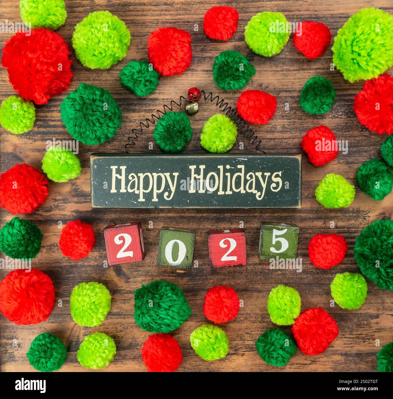Red and green pompoms with wooden blocks and text happy holidays and 2025 on wood Stock Photo