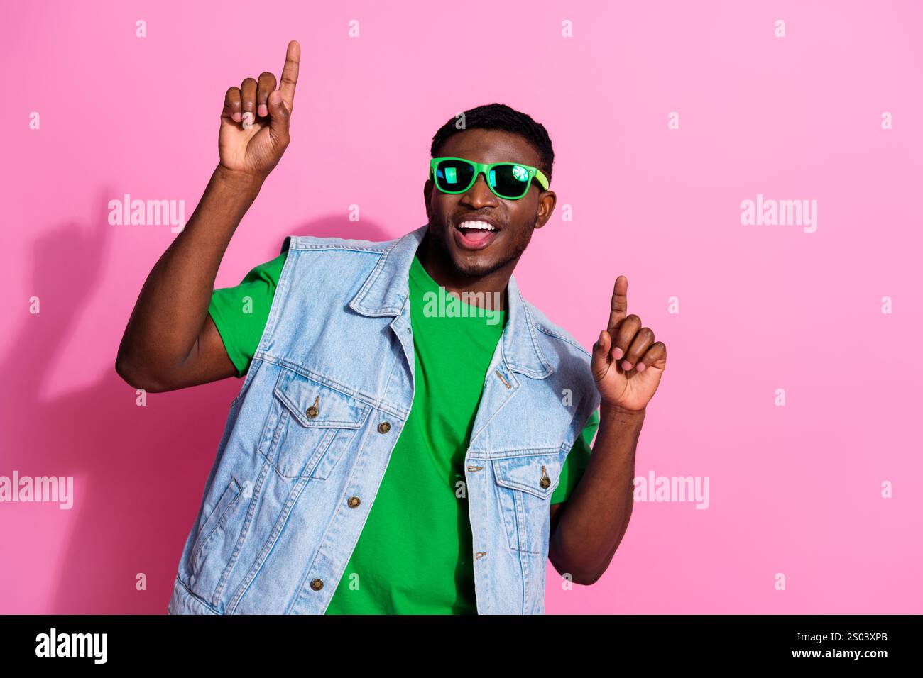 Trendy young man poses in casual denim vest against a vibrant pink ...
