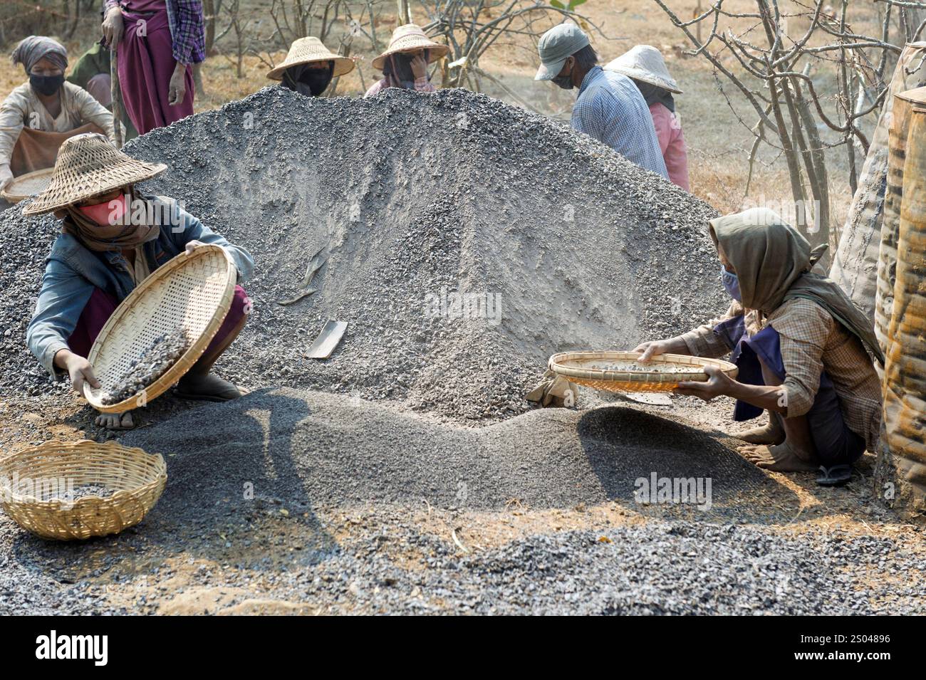 Women in traditional clothing sorting stones with woven baskets at a road construction site in rural Myanmar, Burma Stock Photo