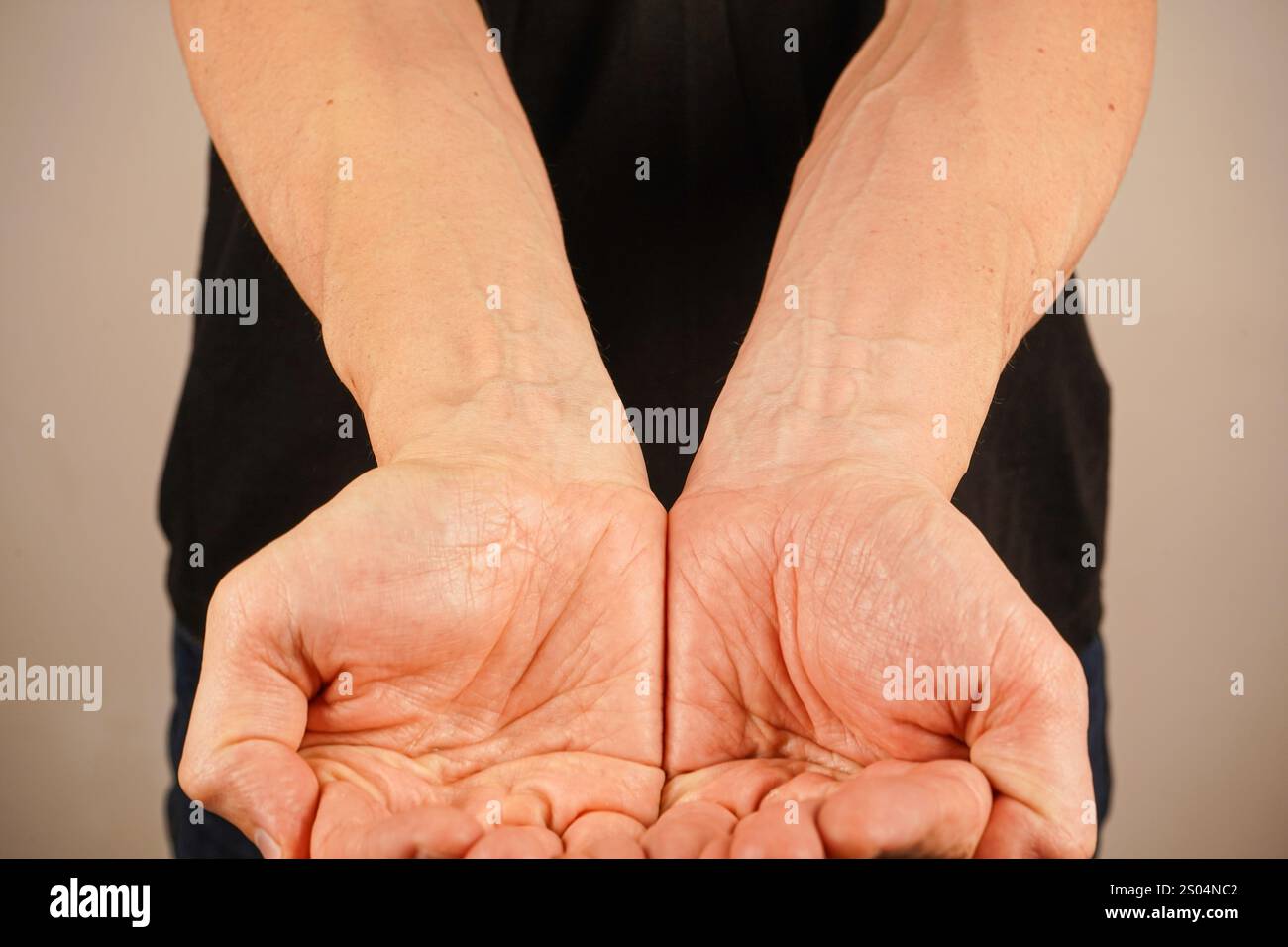 Two palms are cupped together, symbolizing care and offering. Set against a light-colored wall, the minimalist background enhances the emotional depth Stock Photo