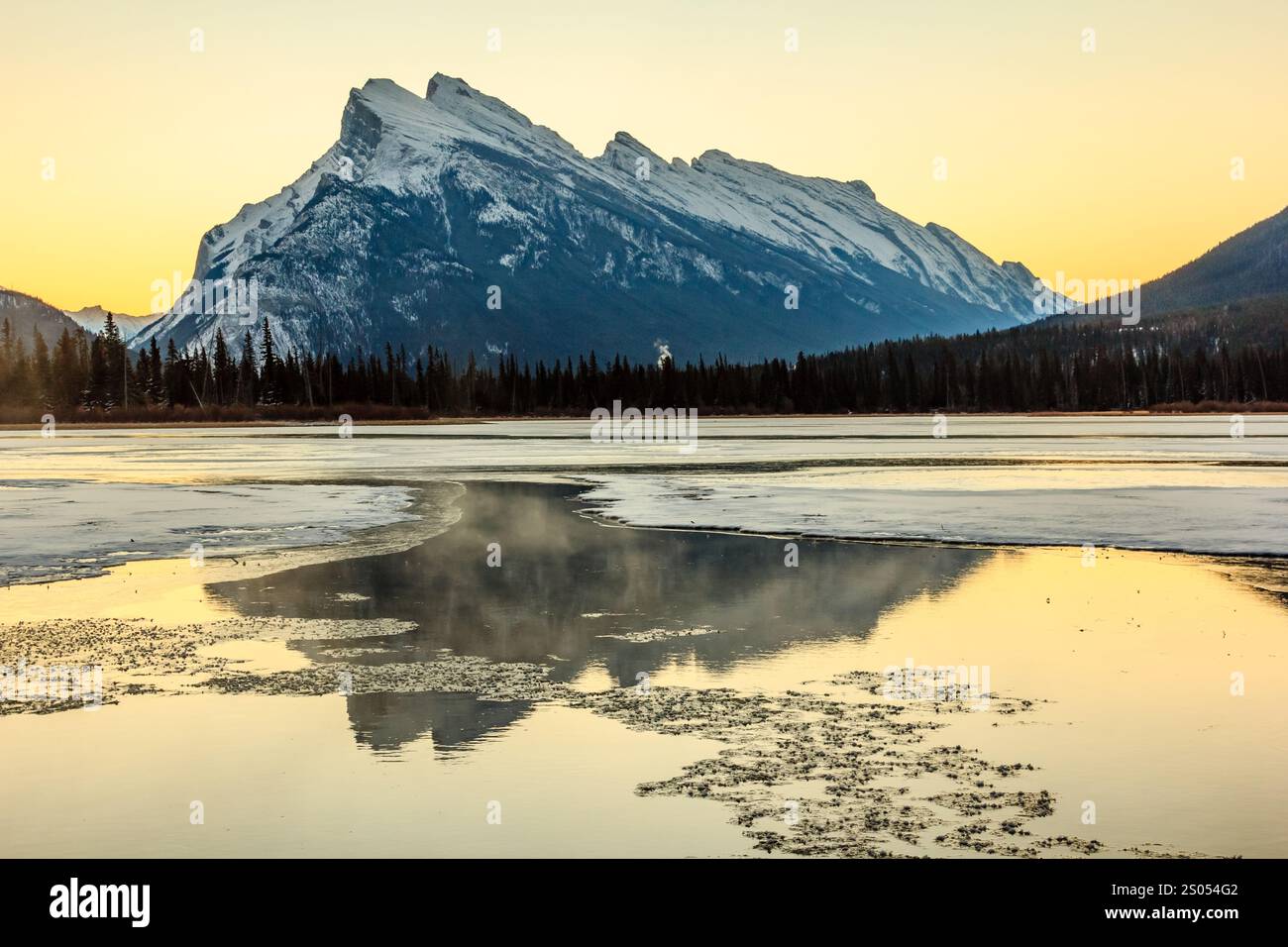 A mountain range is reflected in the water of a lake. The sky is orange ...