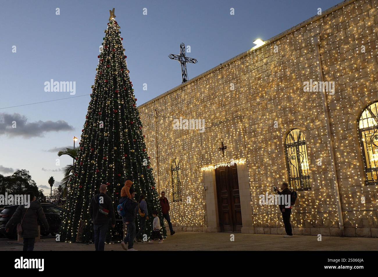 People walk around a decorated Christmas tree and string lights ...