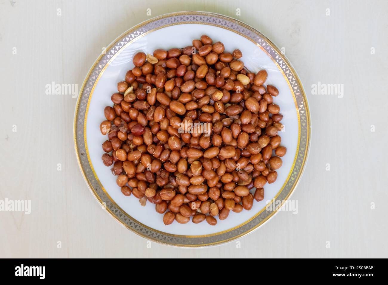 Top view of roasted peanuts in a white plate on a wooden surface. Stock Photo