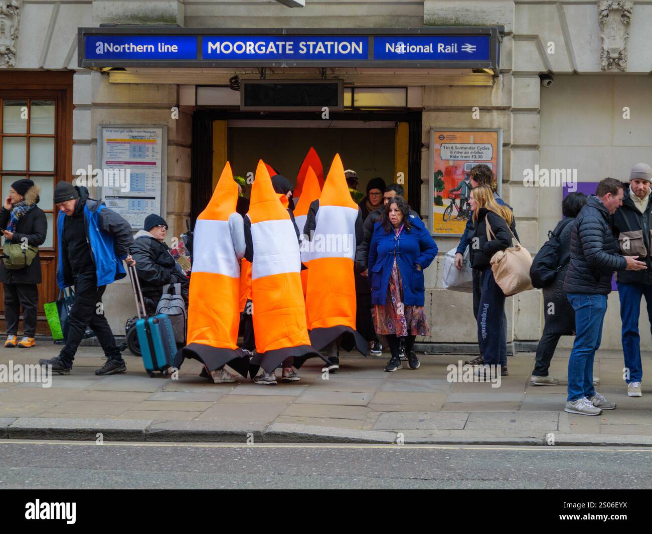 A group of people, dressed as fluorescent traffic cones in fancy dress, entering Moorgate tube station London UK , during the Christmas party season Stock Photo