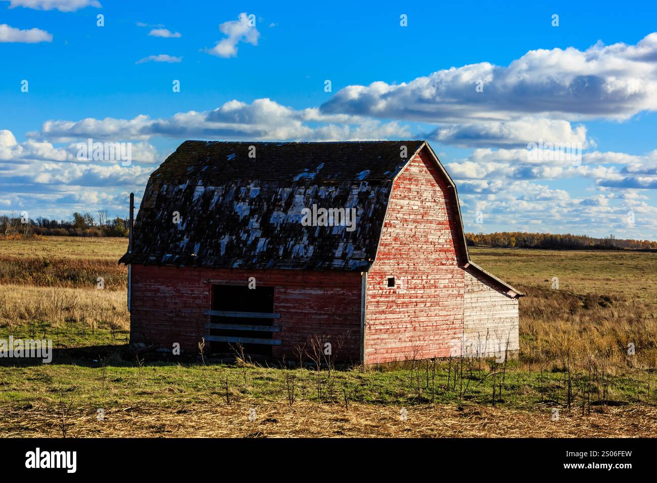 A red barn sits in a field with a blue sky in the background. The barn ...