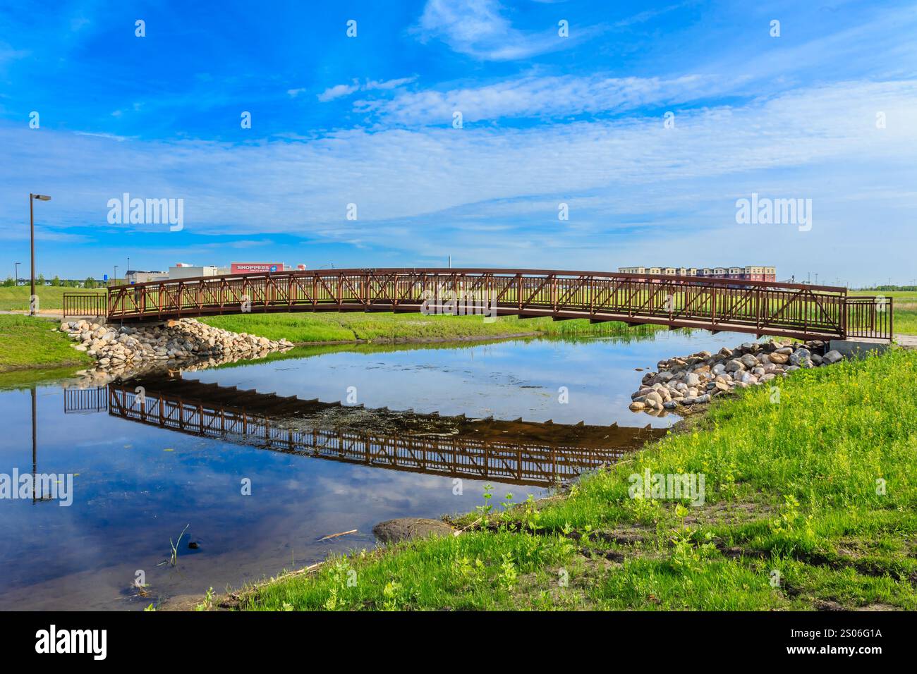 A bridge spans a river, with a green grassy area on either side. The ...