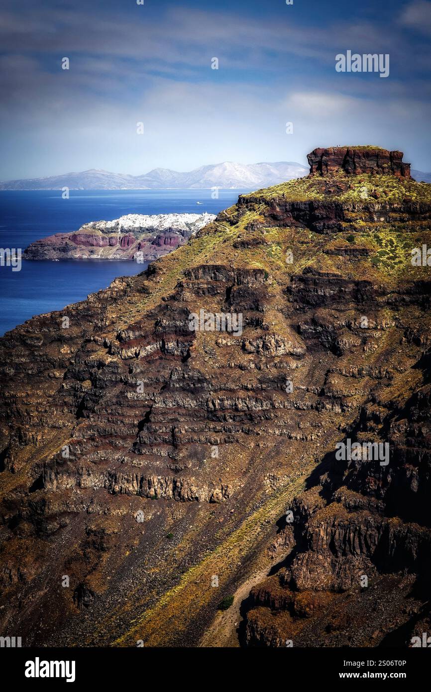 The dramatic cliffs of Skaros Rock dominate the foreground, partially concealing the picturesque village of Oia perched on Santorini's horizon. Stock Photo