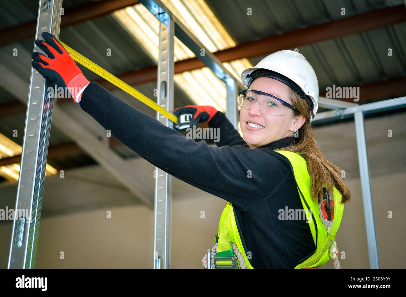 Construction worker using measuring tape while mounting plasterboard in a new building Stock Photo