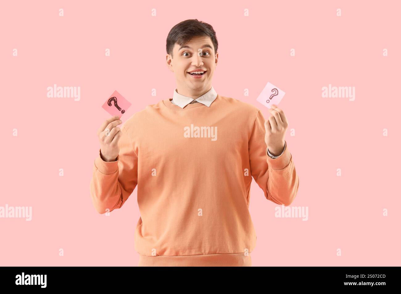 Young man holding sticky notes with question marks on pink background Stock Photo
