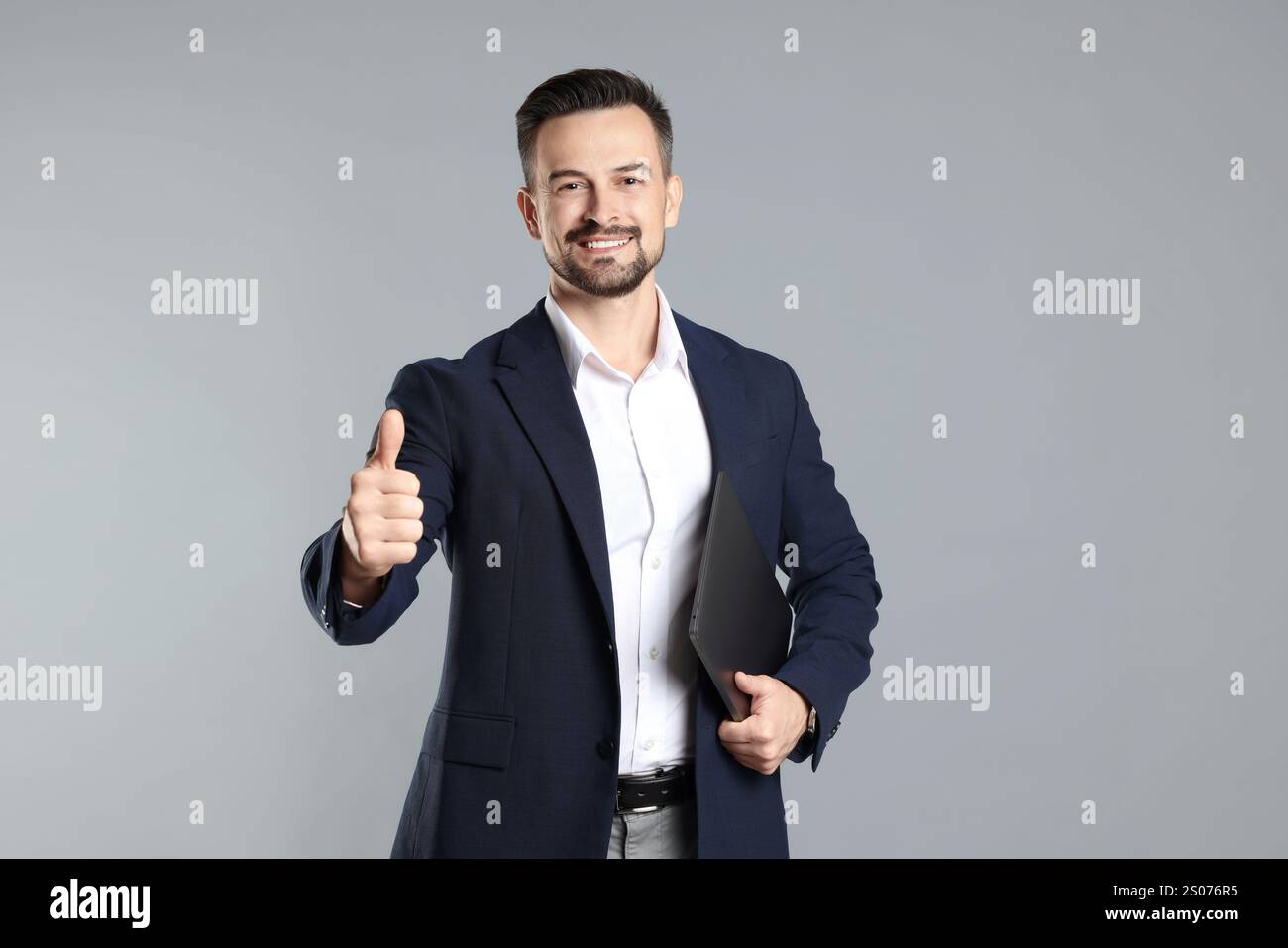 Portrait of smiling banker with laptop showing thumbs up on grey ...