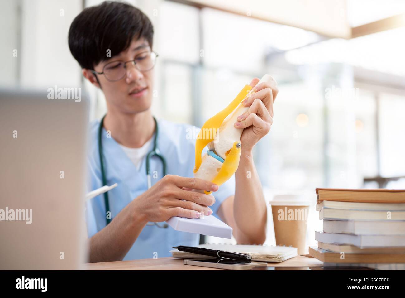 A smart Asian male medical student in scrubs is examining a model of ...