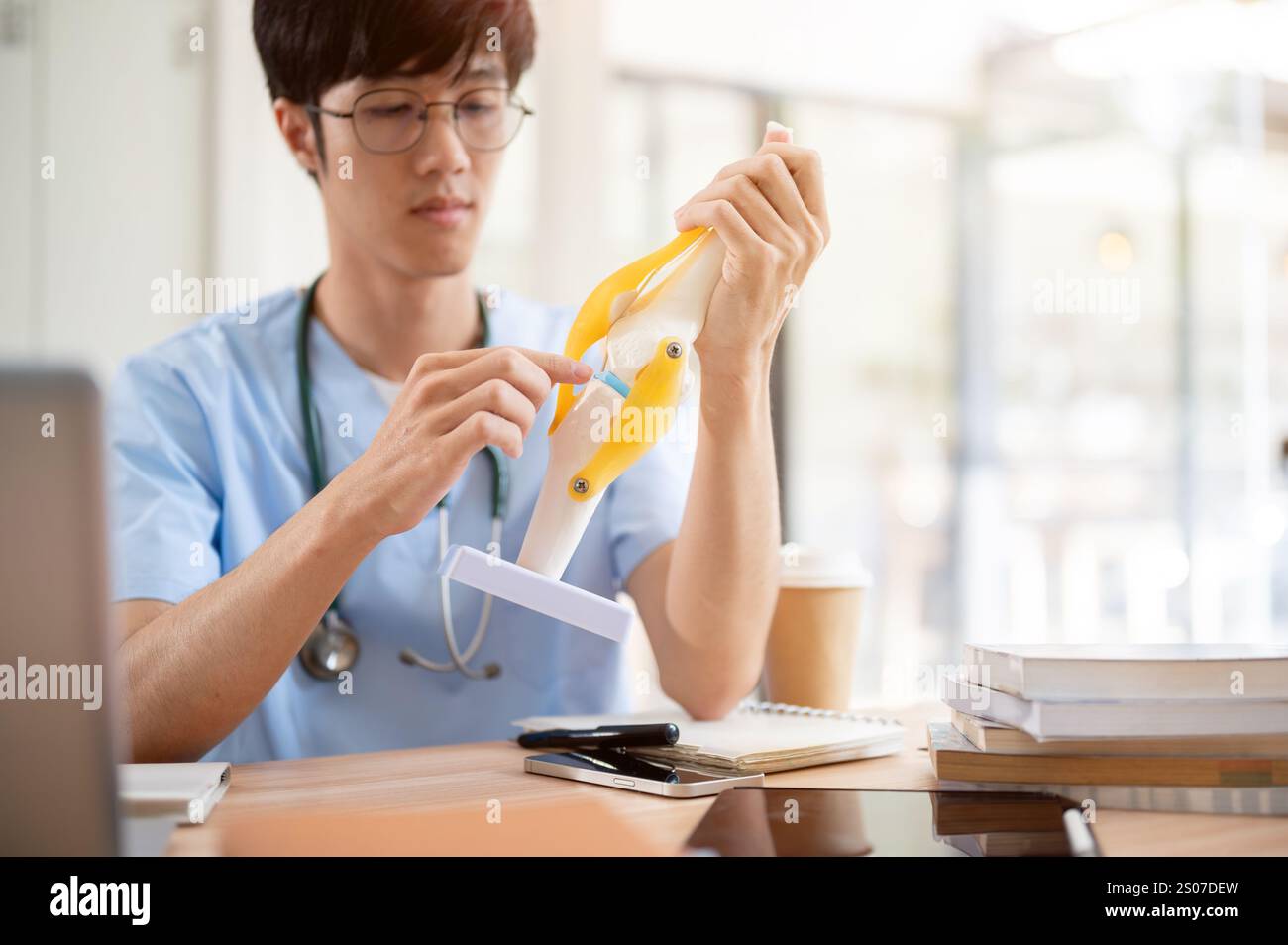 A smart Asian male medical student in scrubs is examining a model of ...