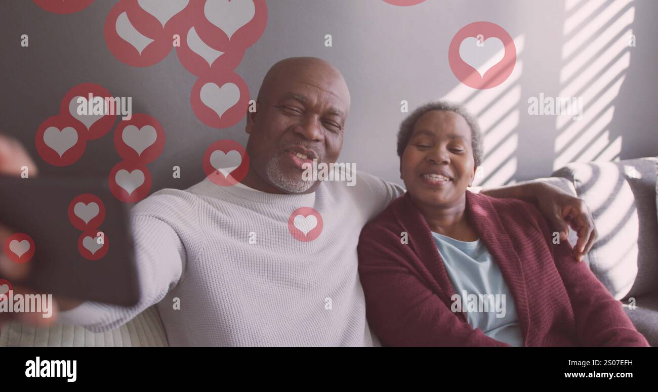Image of hearts over senior african american couple taking selfie at christmas Stock Photo