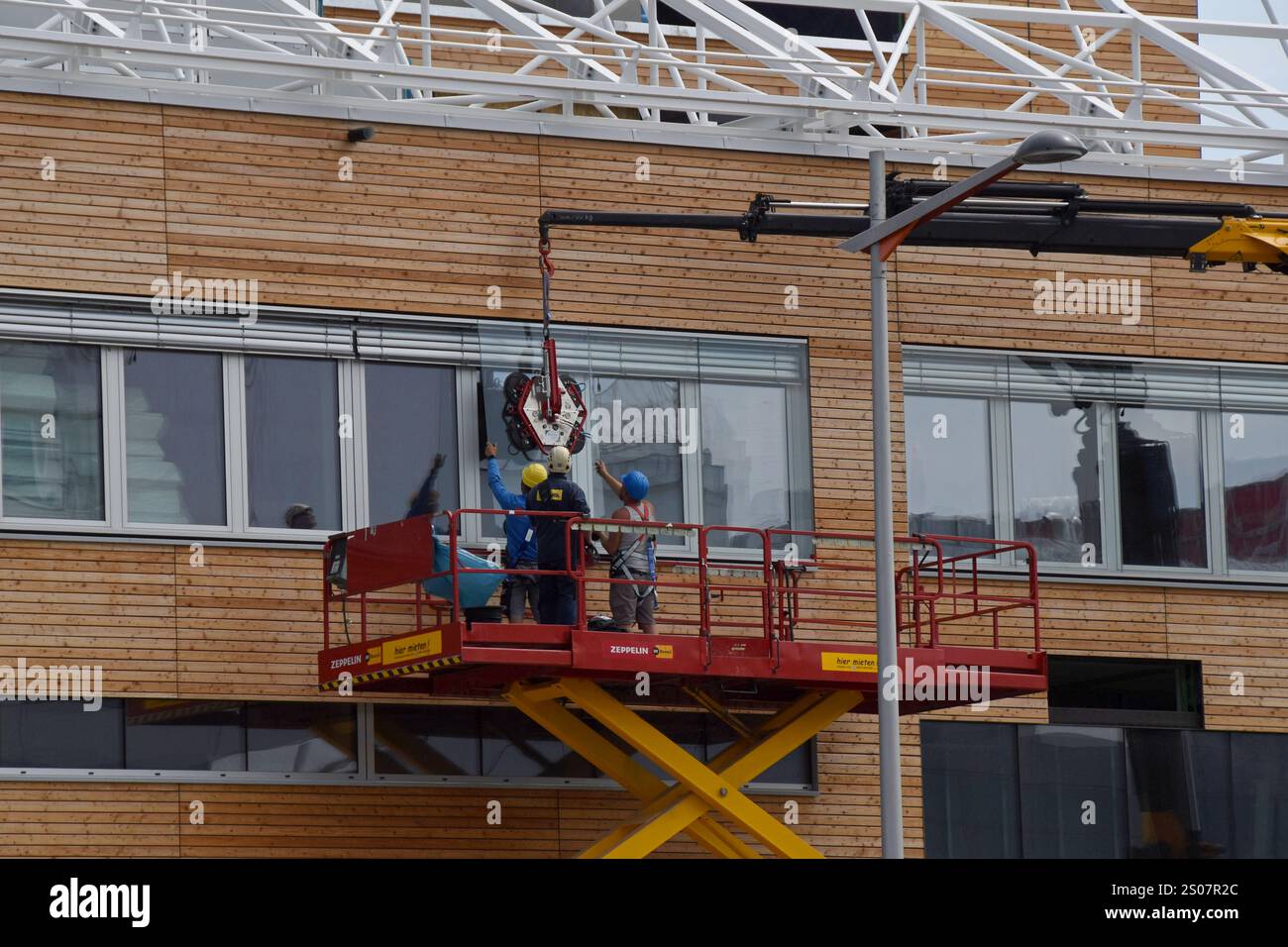 Workers on a building site installing new windows at height at the Village Im Dritten housing development, Vienna, Austria, June 2024 Stock Photo