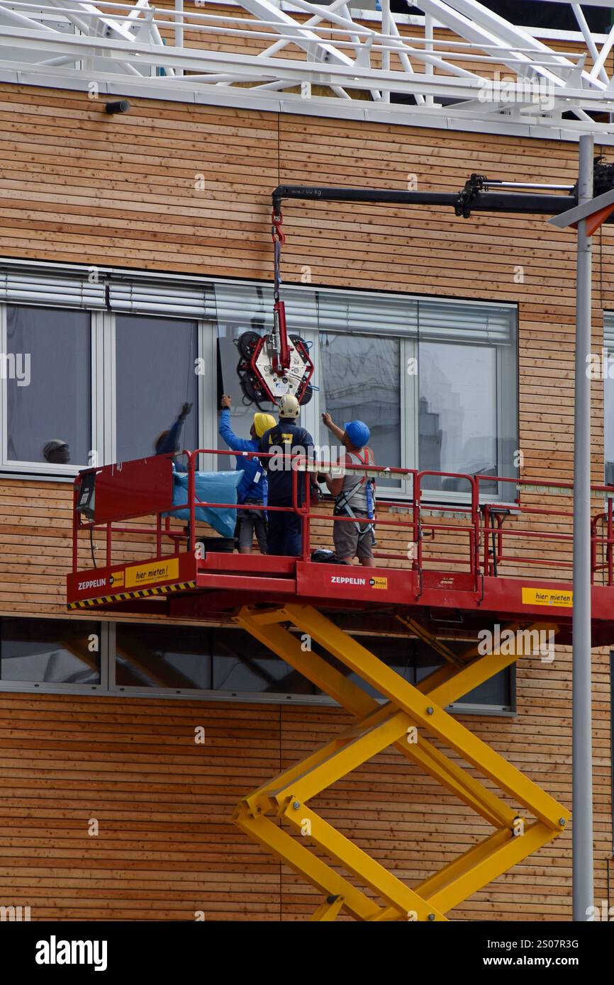 Workers on a building site installing new windows at height at the Village Im Dritten housing development, Vienna, Austria, June 2024 Stock Photo