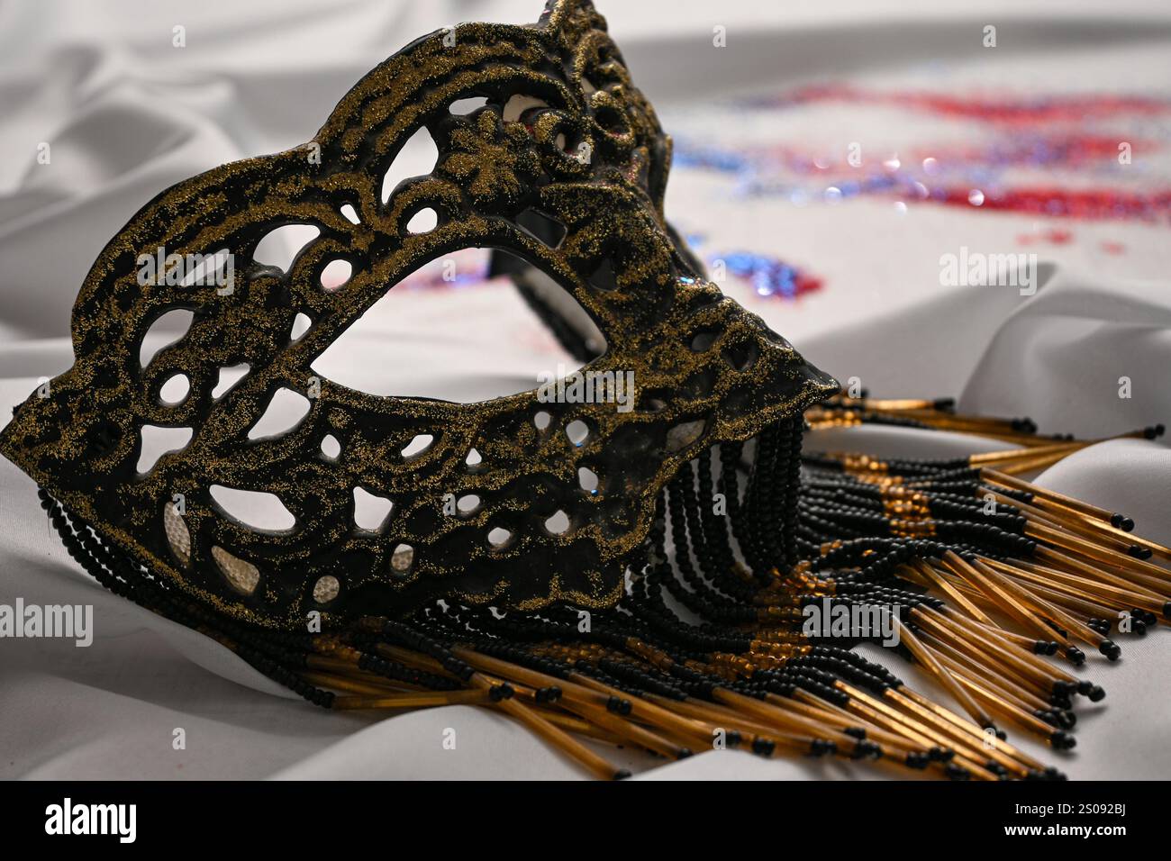 Elegant venetian mask with beads lying on white fabric with red, white ...