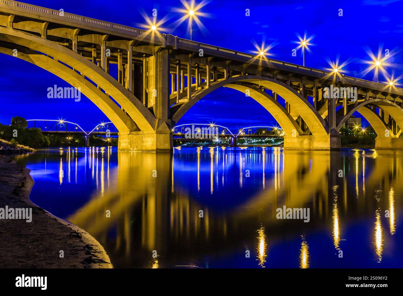 A bridge with lights shining on it. The lights are reflecting on the water. The bridge is lit up at night Stock Photo