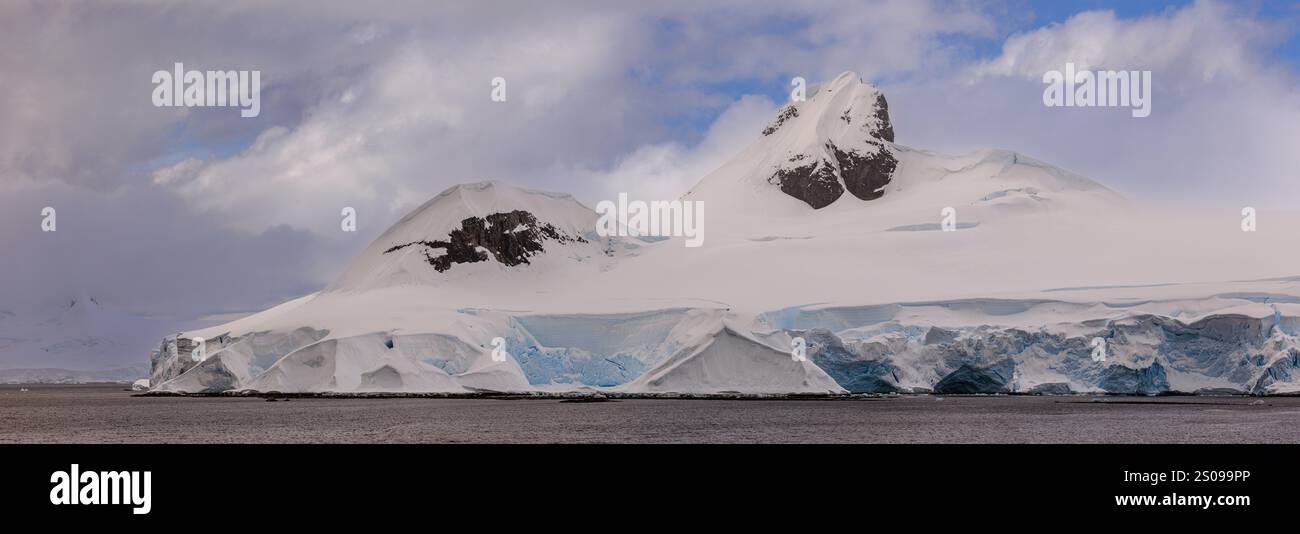 panoramic landscape of sunlight on the snow of the two rocky mountain tops of jacques peaks at the entrance to bancroft bay on the antarctic peninsula Stock Photo