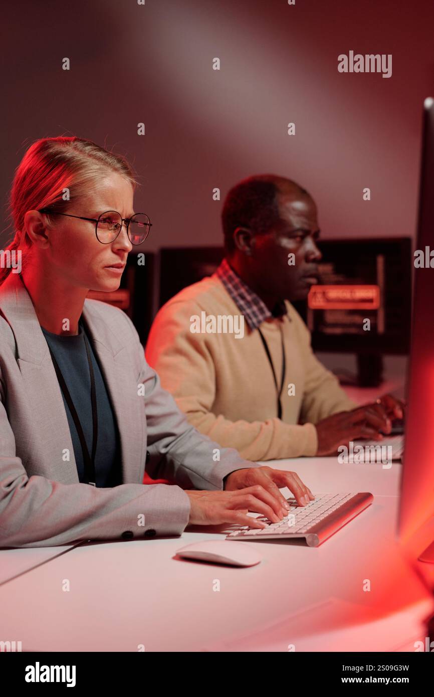 Young IT support manager in formalwear looking at computer screen while solving technical problem against male coworker Stock Photo