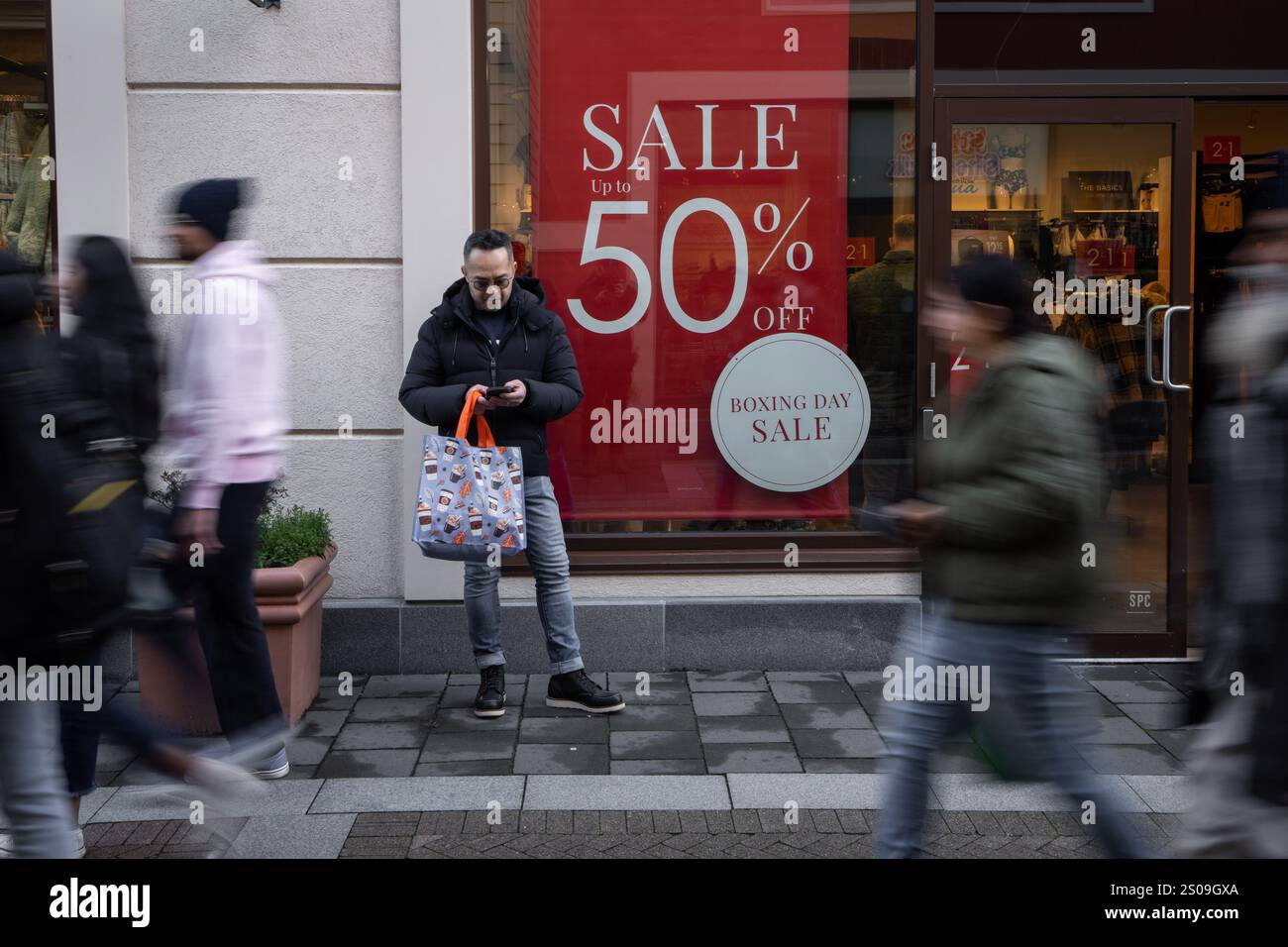 A man waits outside a store advertising a sale of up to 50 per cent off
