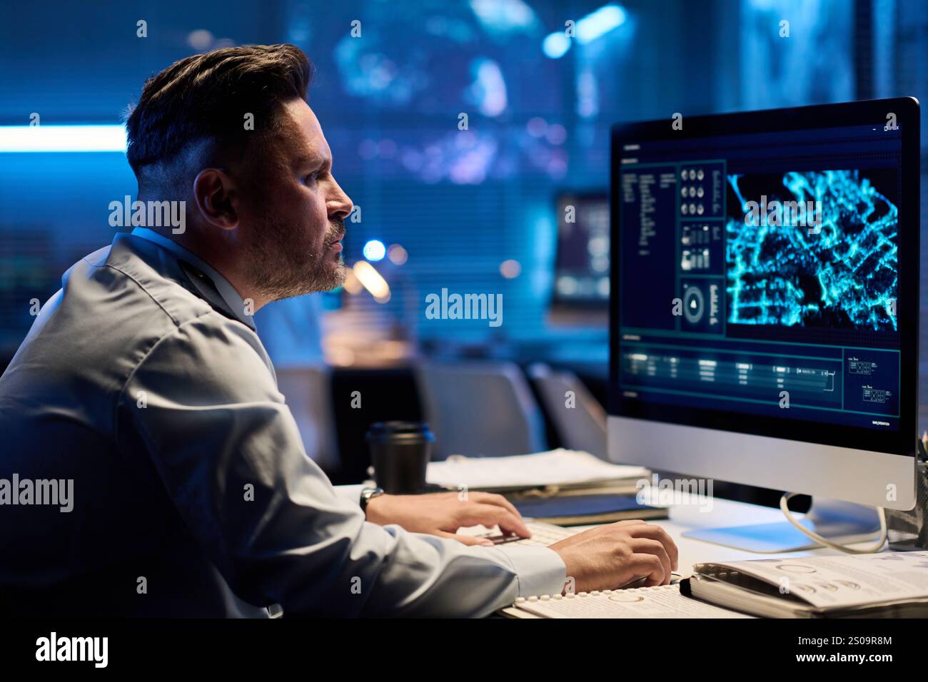 Serious operator in uniform learning data on desktop computer screen and clicking mouse while sitting by workplace Stock Photo
