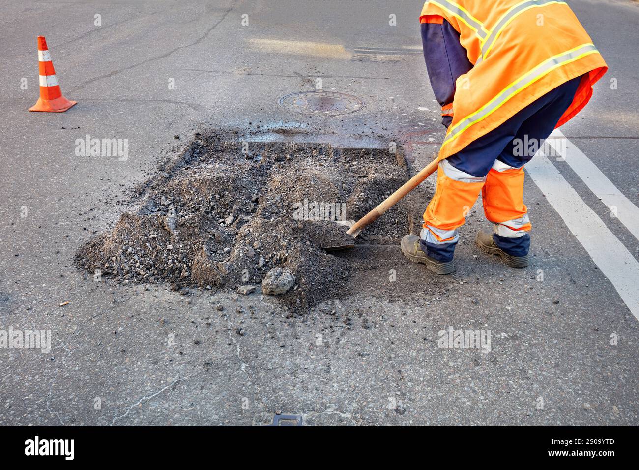 Road repair crew diligently works to fix pothole during sunny afternoon Stock Photo