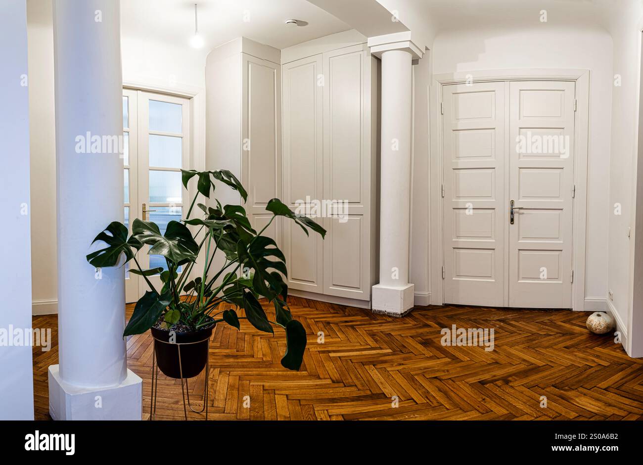 The room features a polished herringbone wooden floor, white walls, and ...