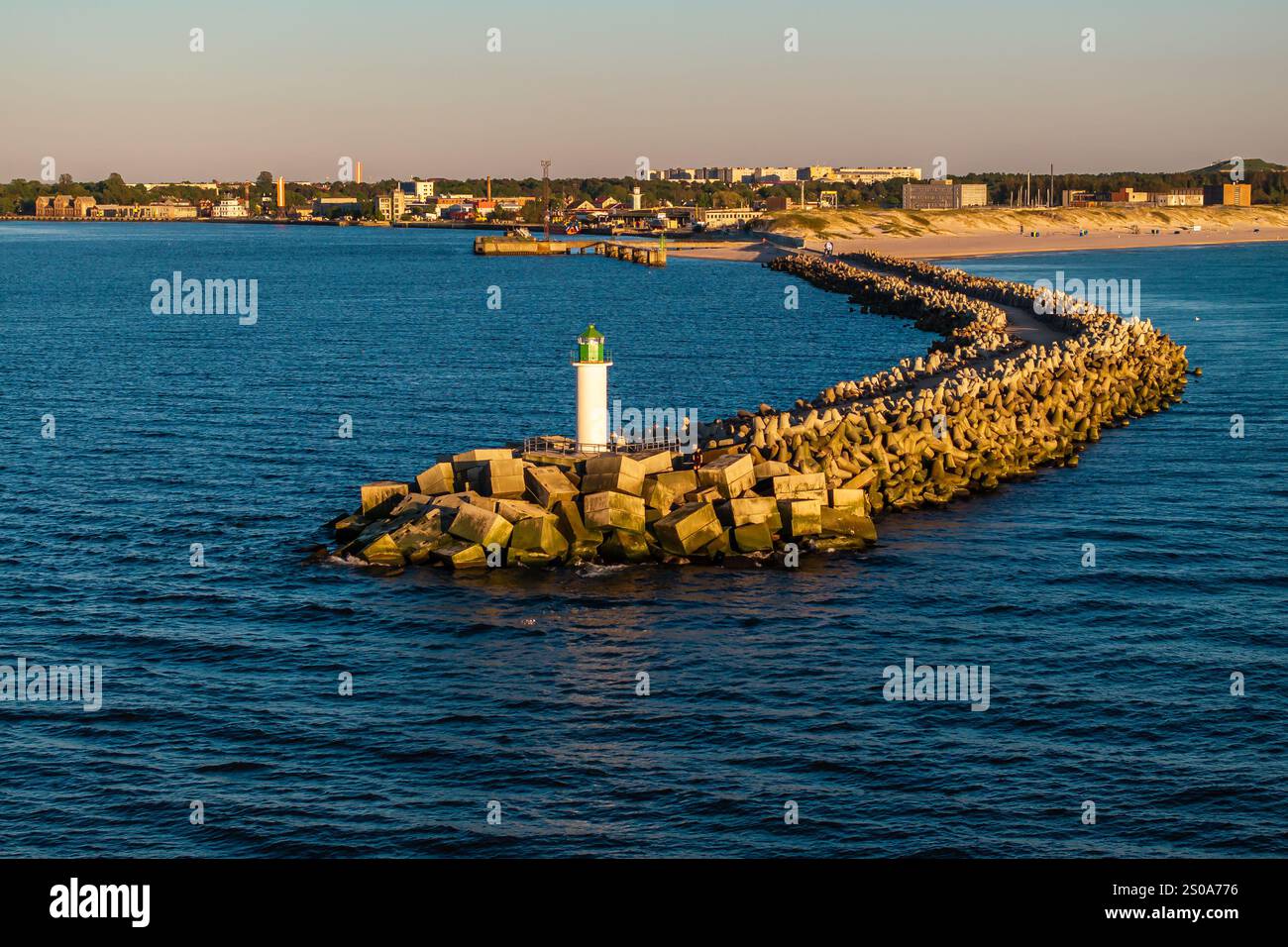 A long breakwater with a white lighthouse and green top extends into ...