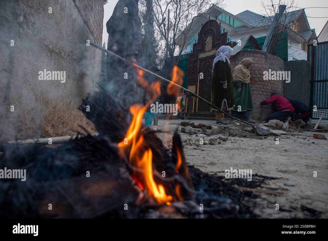 A Kashmiri family is seen heating frozen drinking water pipes by lighting a fire on them during an intense cold winter day in Srinagar. The capital city, Srinagar, has recorded a low of minus 7.3 degrees Celsius (18.86 degrees Fahrenheit) on Thursday night as the local weather office has predicted a possibility of light snowfall over the higher reaches on Friday and Saturday as a Western Disturbance is set to impact the Himaliyan region. Kashmir is currently under the grip of ‘Chillai-Kalan, ' considered the harshest 40-day period of winter, which started on December 21. The fall in the mercur Stock Photo