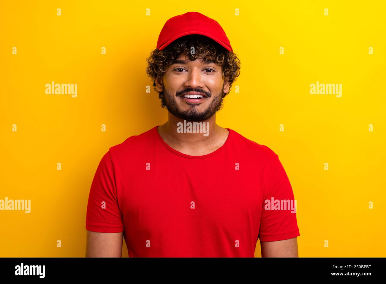 Stylish young man in red shirt and cap smiling against a vibrant yellow ...