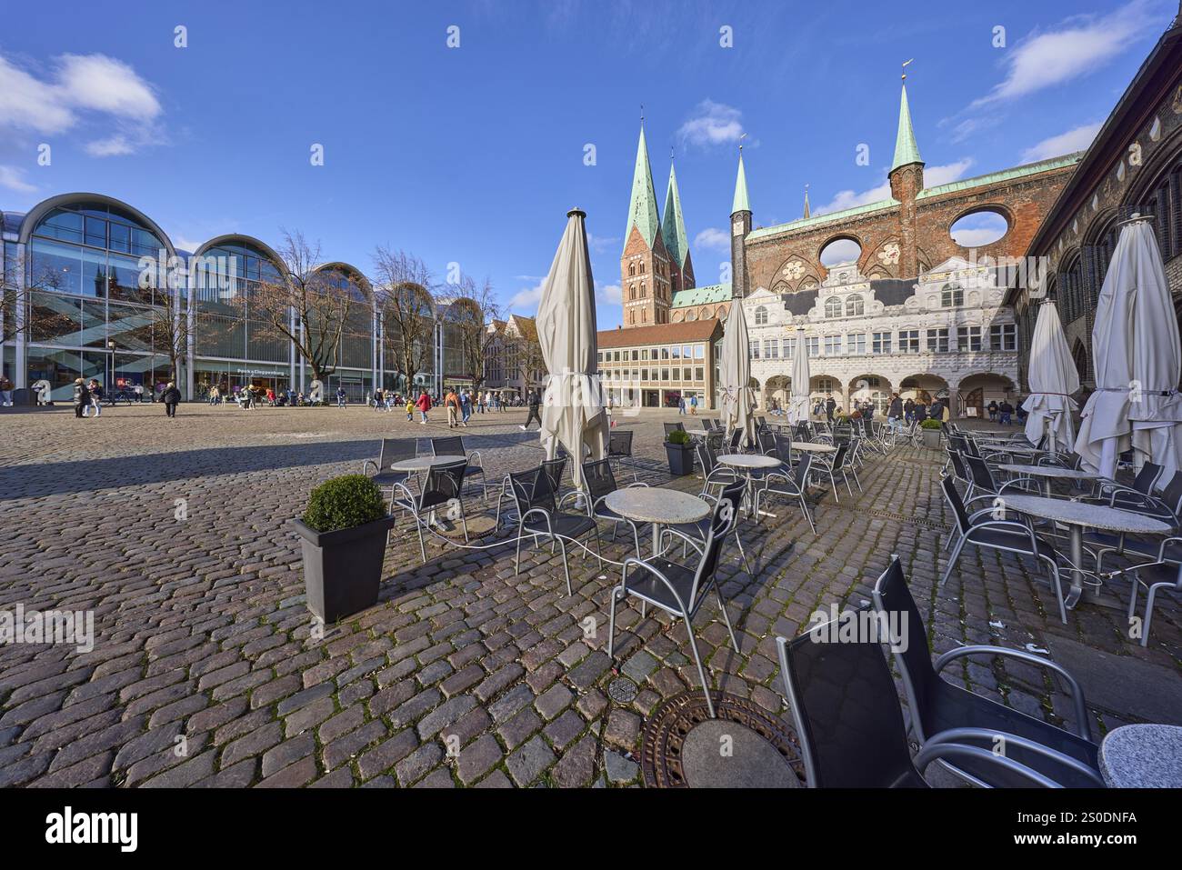 Church tower of St. Marien zu Luebeck, outdoor area of Cafe Niederegger - arcade cafe with tables, chairs and parasols, modern architecture with a b Stock Photo