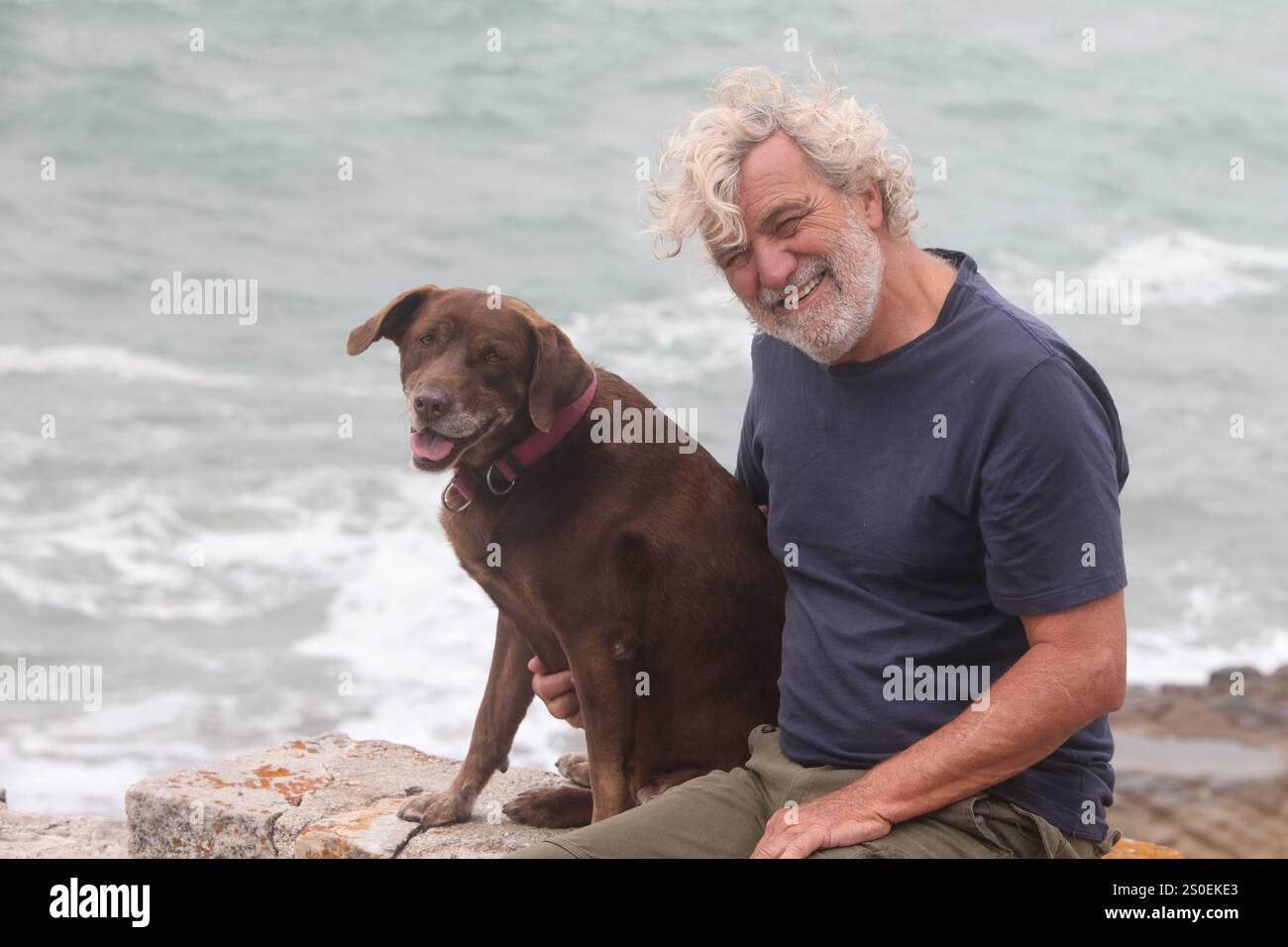 portrait of senior latino man bonding with his dog outdoors with ocean ...