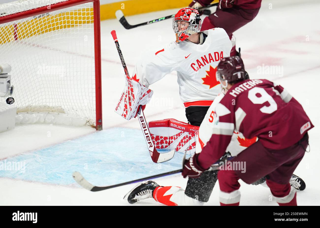Latvia's Eriks Mateiko (9) scores on Canada goaltender Jack Ivankovic