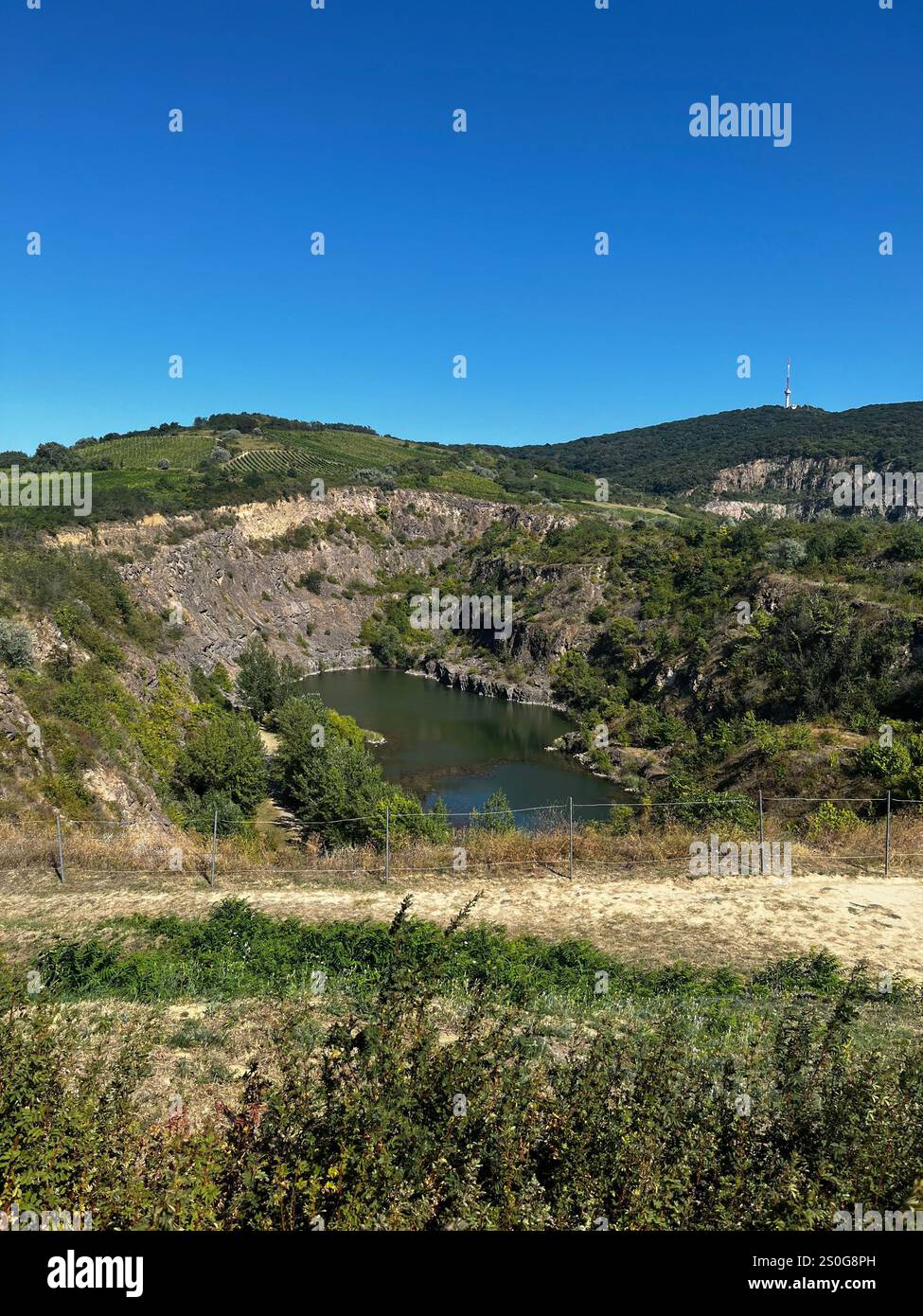 The image shows a scenic landscape featuring a small lake or pond surrounded by rocky cliffs and lush greenery. - Smartphone Captured Stock Image