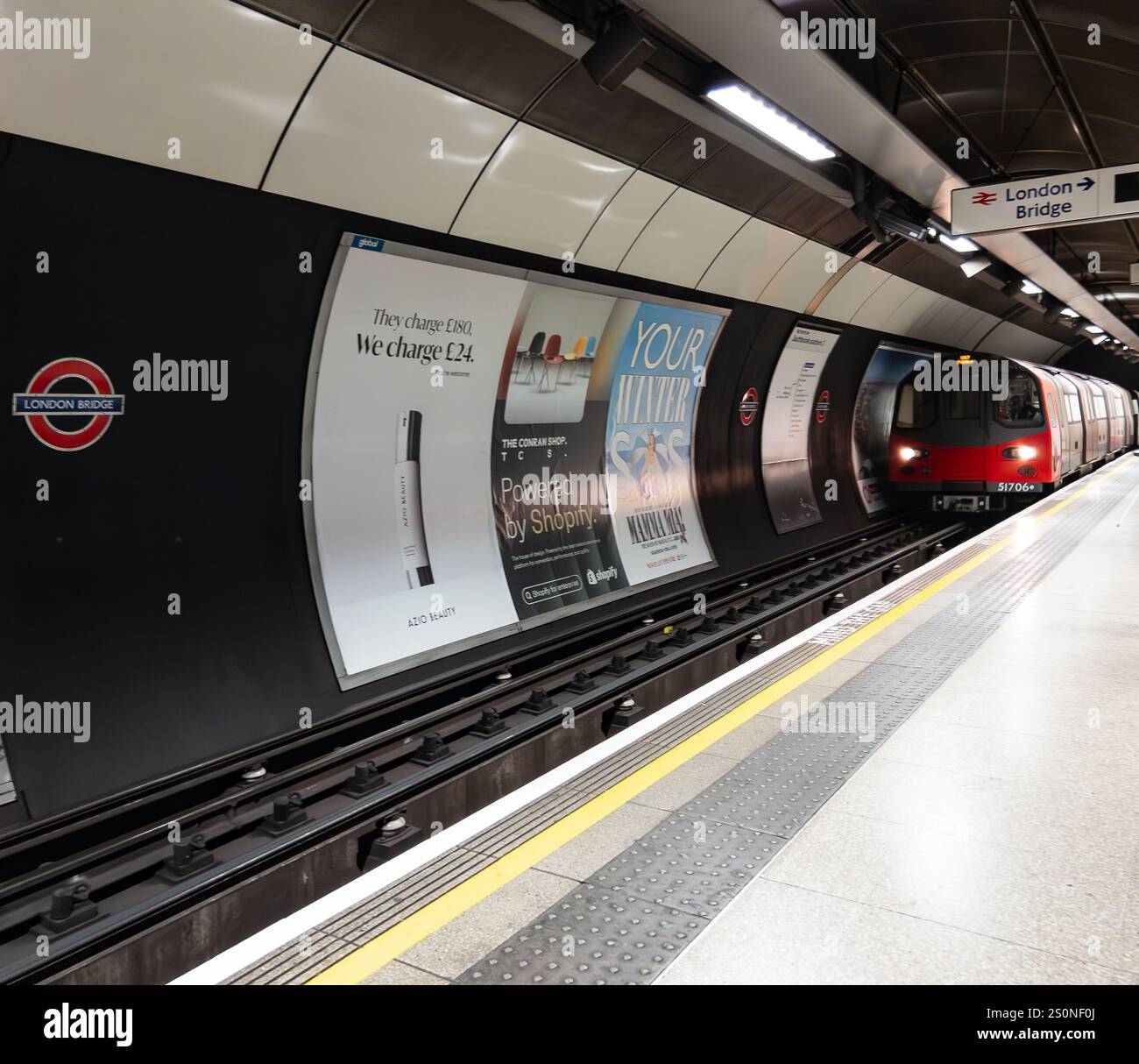 Red train arriving at an underground station with platform posters in the London Bridge subway station - Smartphone Captured Stock Image