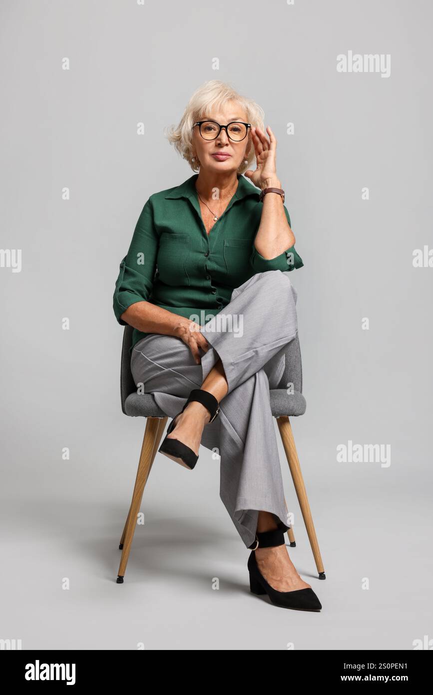 Beautiful senior woman sitting on chair against light grey background ...