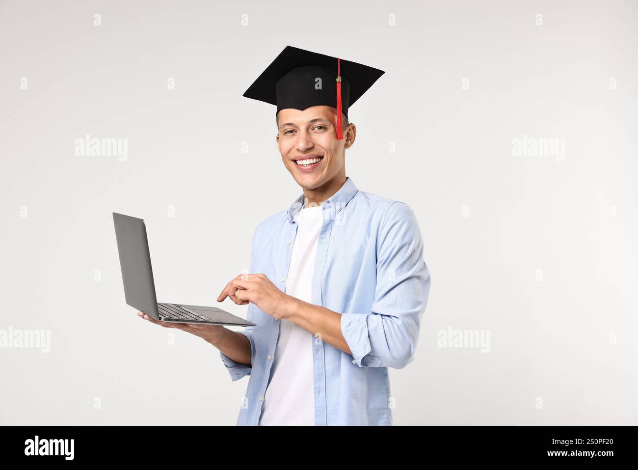 Happy student with laptop after graduation on light grey background ...