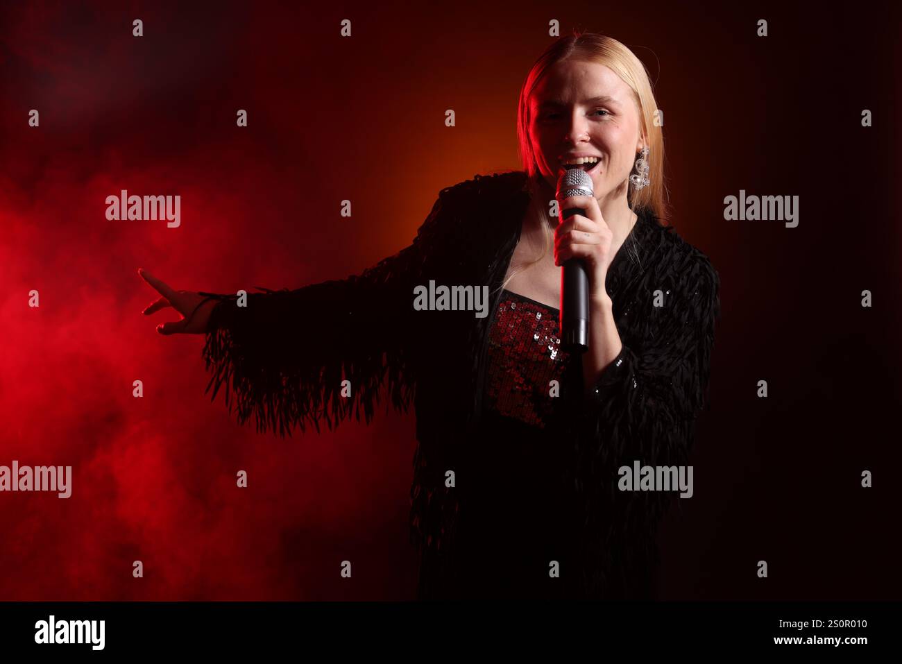 Beautiful singer performing on dark background with red light and smoke ...