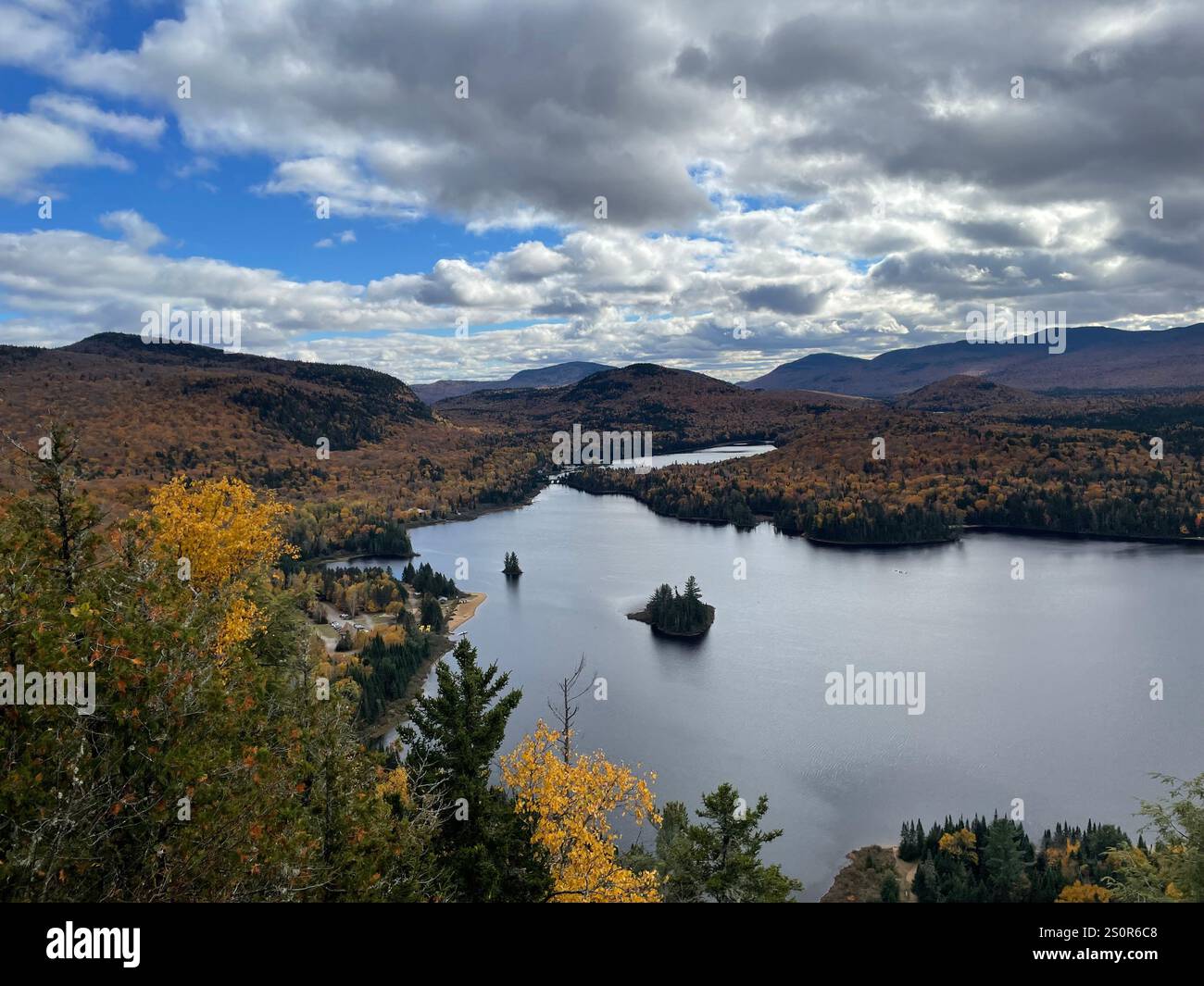 Scenic autumn landscape featuring a calm lake, forested hills, and colorful fall foliage under a partly cloudy sky - Smartphone Captured Stock Image