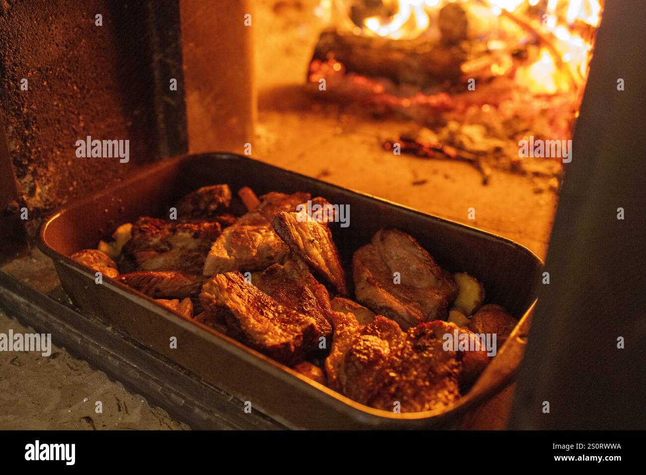 Roasted Meat and Vegetables in a Baking Dish Near Glowing Flames Stock Photo