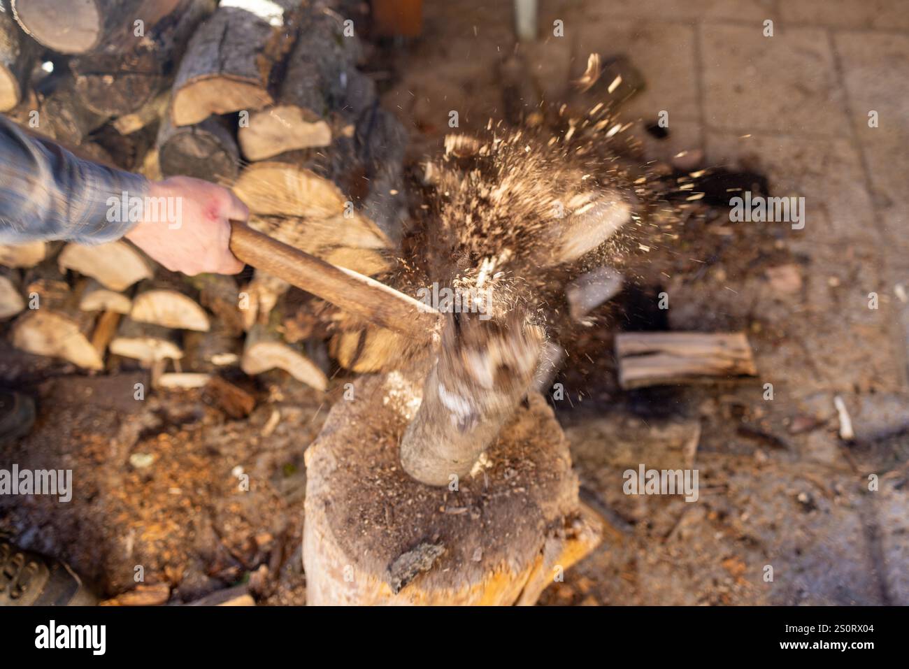 A dynamic action shot of a man splitting a log with an axe on a tree stump. Stock Photo