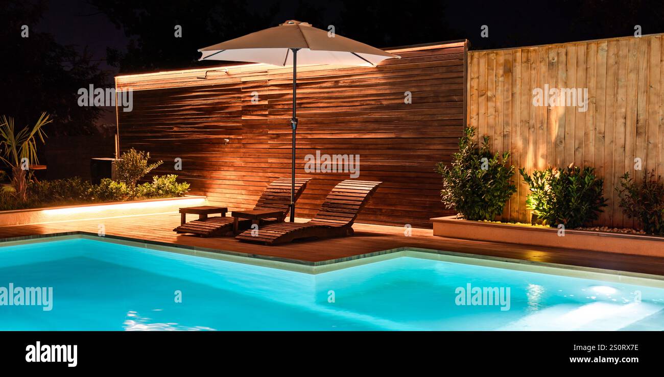 Modern illuminated swimming pool with wooden lounge chairs and a cozy ...