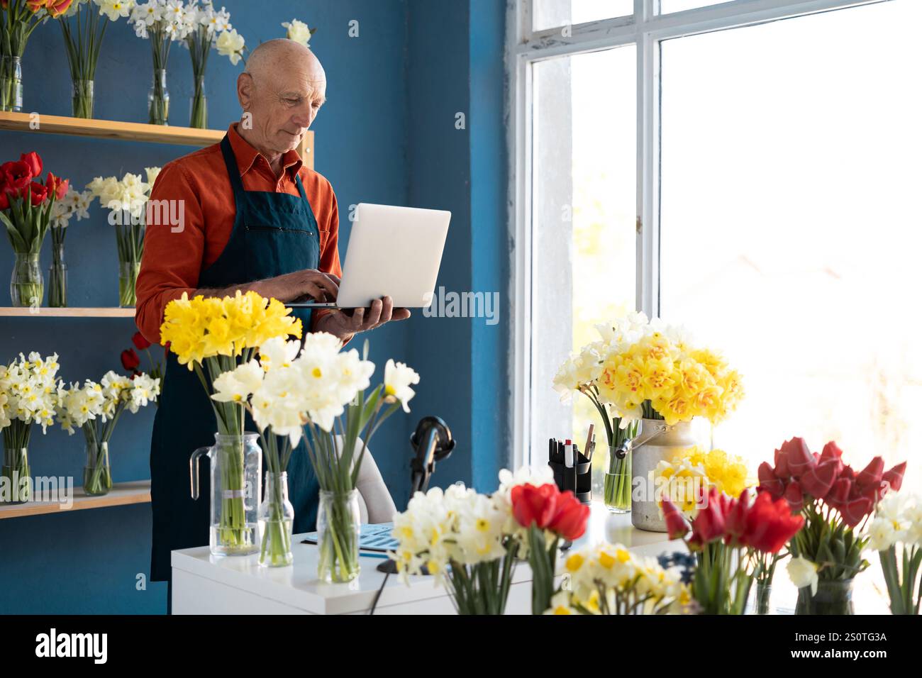 male florist is standing holding laptop in his hands. The daily routine ...