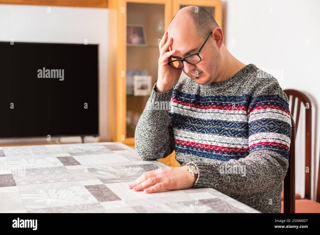 A bald adult male leaning against a table with his head resting on one of his hands and a sad look on his face. Stock Photo