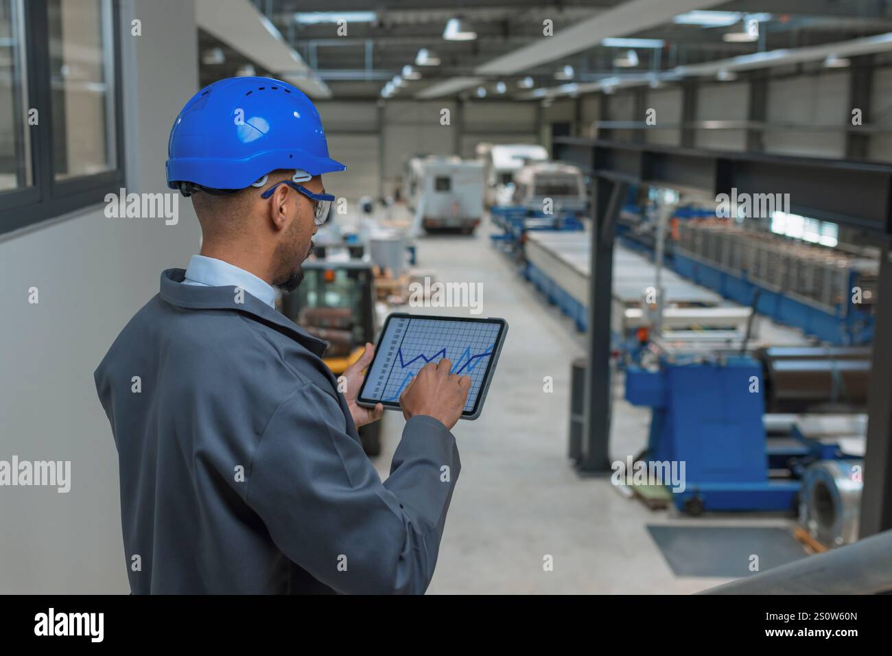 Young engineer programmer using tablet and graphs data to check factory machinery production and work procedure, rear view. Industry career concept. Stock Photo