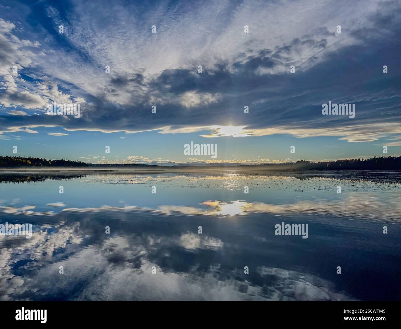 A tranquil lake reflecting the sky's dramatic clouds and sunlight, surrounded by forested hills. Ideal for nature and landscape photography. - Smartphone Captured Stock Image