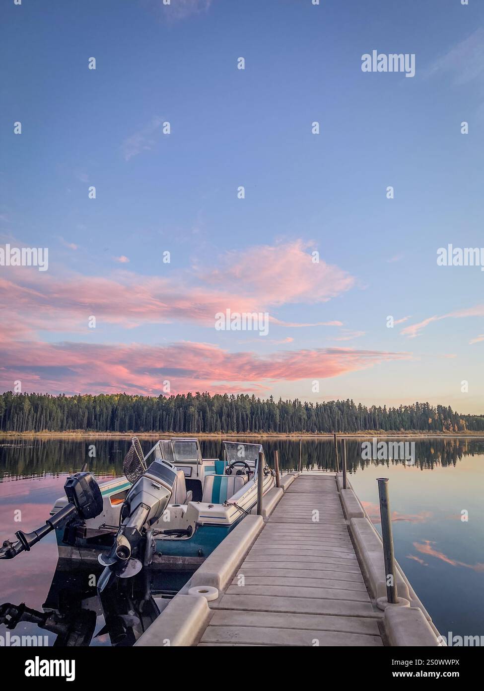 A small motorboat docked on a calm lake during sunset, with vibrant reflections on the water and a forested horizon under a colorful evening sky. - Smartphone Captured Stock Image