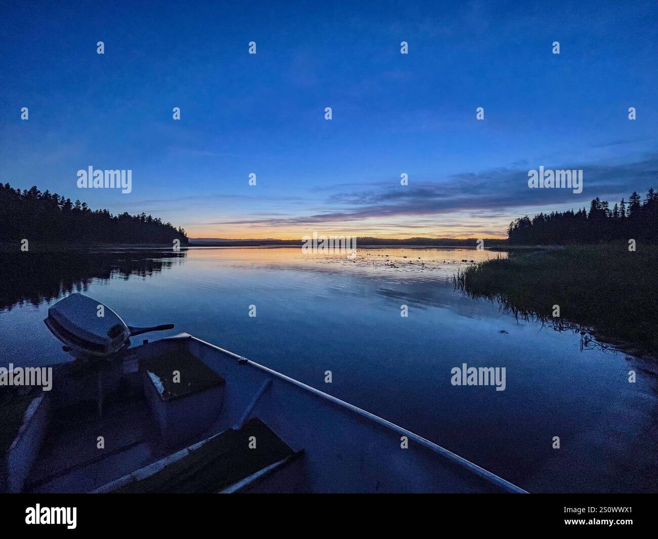 A serene evening on a calm lake with a small boat, twilight sky, and wilderness in the background. - Smartphone Captured Stock Image