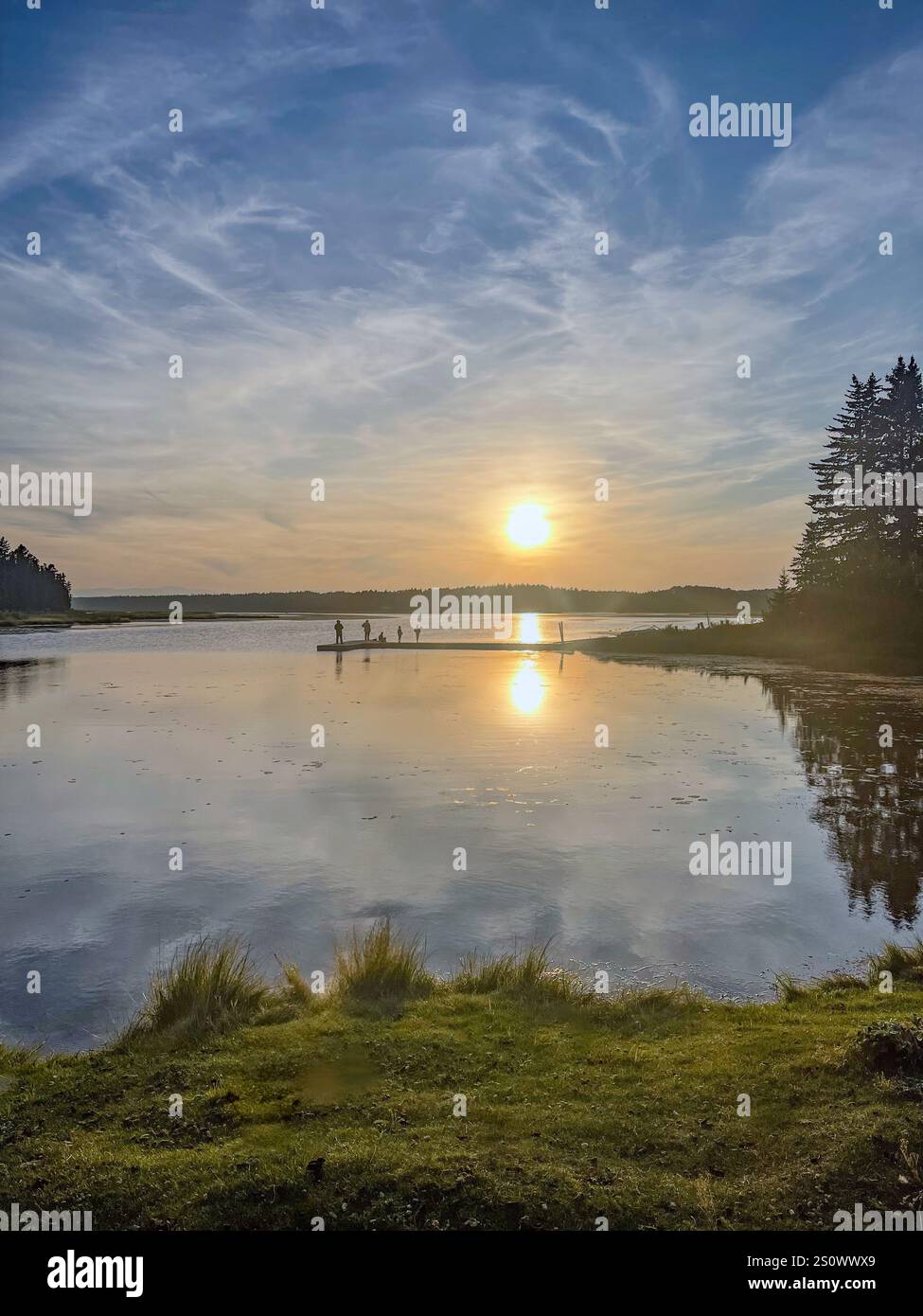 A vibrant sunset casts colorful reflections on a calm lake, with a dock visible in the distance, creating a serene and picturesque scene. - Smartphone Captured Stock Image
